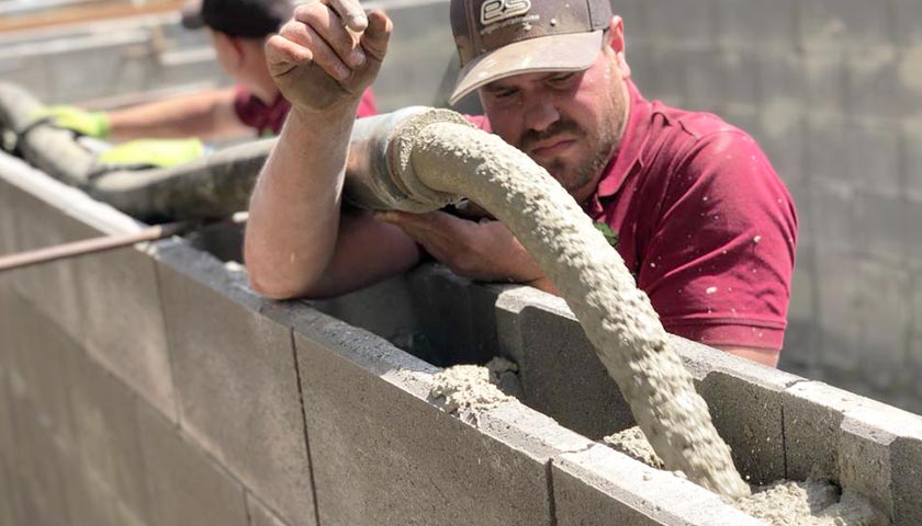 Mitarbeiter gießen Beton in eine Poolkonstruktion